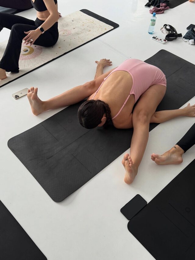 Someone folded all the way forward on a mat, face down, the class going on around her.